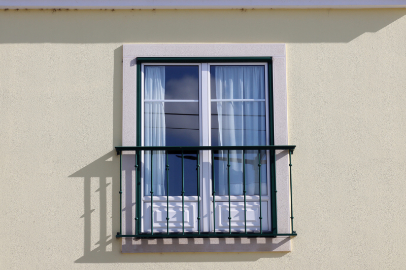 Large window with metal railing outside. Window with French balcony on yellow wall.